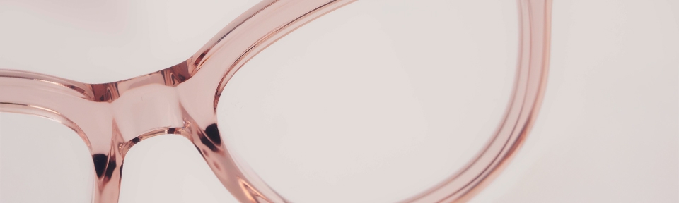 Nahaufnahme eines Brillengestells in zartem Roséton auf hellem Hintergrund, die transparente Kunststoffstruktur ist deutlich sichtbar.