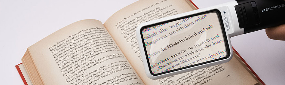 Aufgeschlagenes Buch wird mit einer digitalen Lupe von Eschenbach vergrößert betrachtet.
