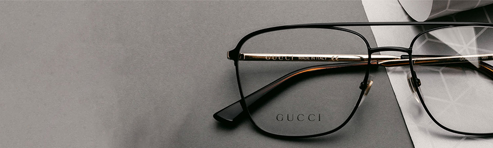 Eine schwarze Herrenbrille von Gucci liegt auf einer dunklen Fläche.