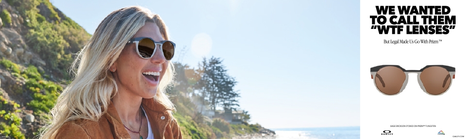 Eine Frau trägt eine Oakley Sonnenbrille vor einem Berg am Strand.