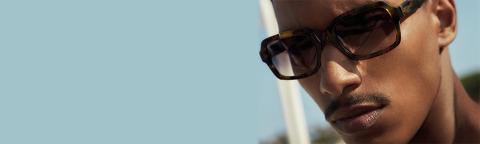 Ein Mann trägt eine Scotch & Soda Sonnenbrille vor einem blauen, freien Himmel.