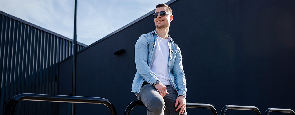 Ein Mann trägt eine Piloten-Sonnenbrille vor einer schwarzen Wand.