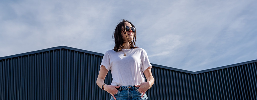 Ein Frau trägt eine Aviator-Sonnenbrille unterm blauen Himmel.