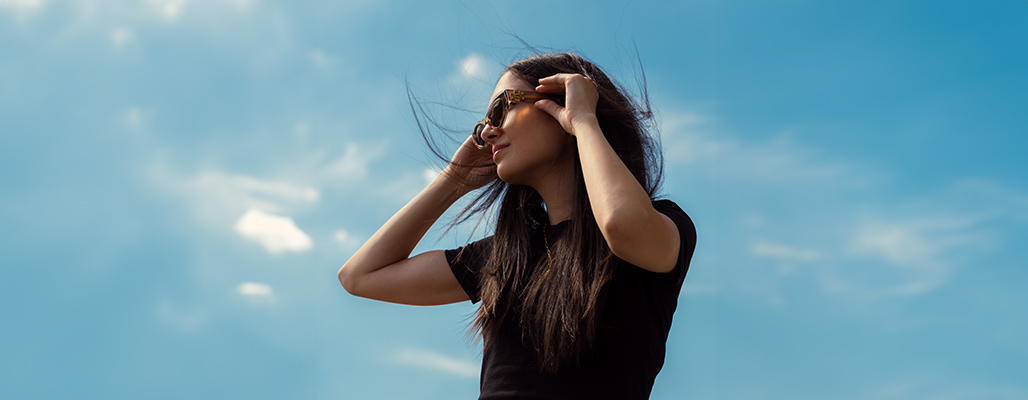 Eine Fraut trägt eine Bold-Sonnenbrille vor blauen Himmel.