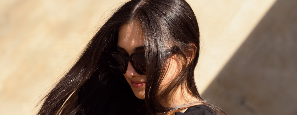 Nahaufnahme einer Frau, welche eine Bold-Sonnenbrille vor einer gelben Wand trägt.