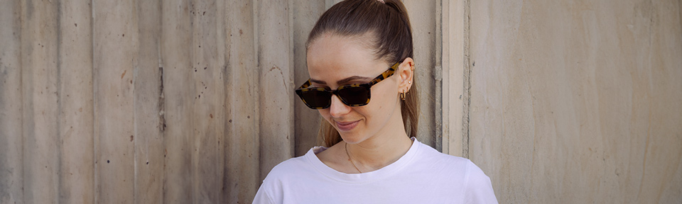Eine Frau trägt eine havanna Leopardenmuster-Sonnenbrille vor einer Wand.