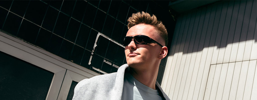 Ein Mann trägt eine schnelle Brille vor einer Wand.