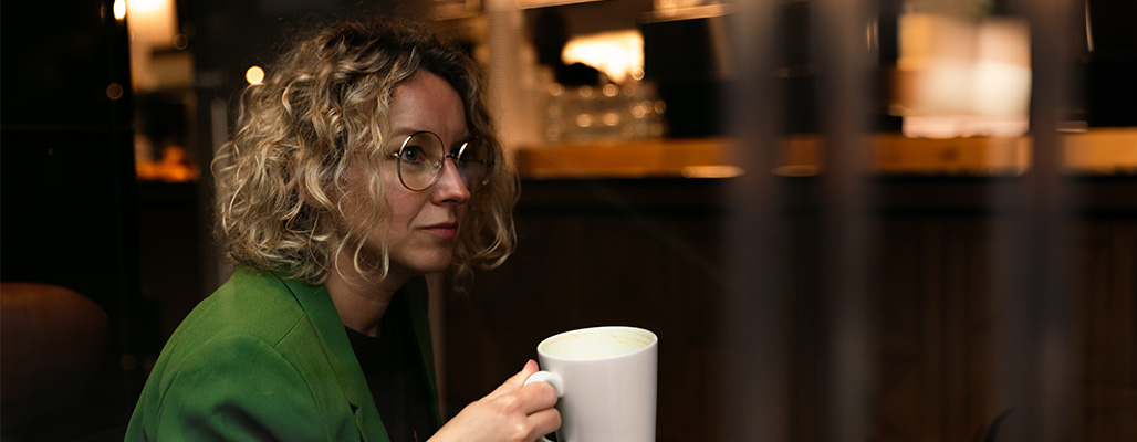 Eine Frau trägt eine Windsor-Brille während sie eine weiße Tassse hält.