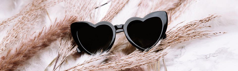 Eine Hochzeits-Sonnenbrille in Herzform liegt auf einem hellen Untergrund.