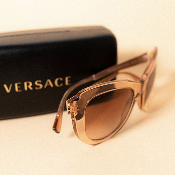 Designer-Sonnenbrille in warmem Farbton neben einem Brillenetui mit Versace-Logo.